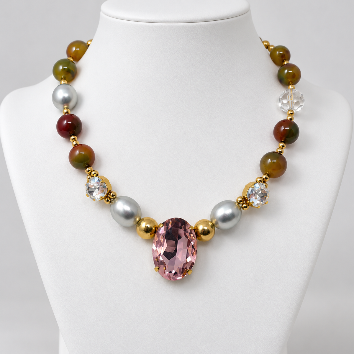 Agate and pearl necklace with a pink oval crystal displayed on a white jewelry bust.