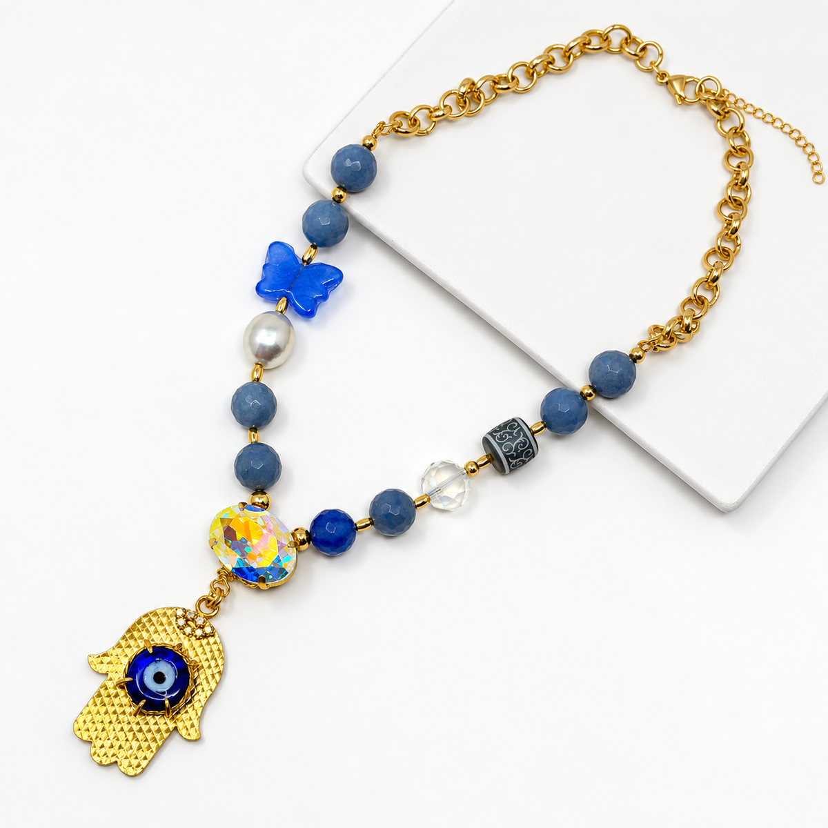 Blue aventurine necklace with a gold-tone hamsa pendant, blue evil eye, and oval iridescent crystal laid flat.