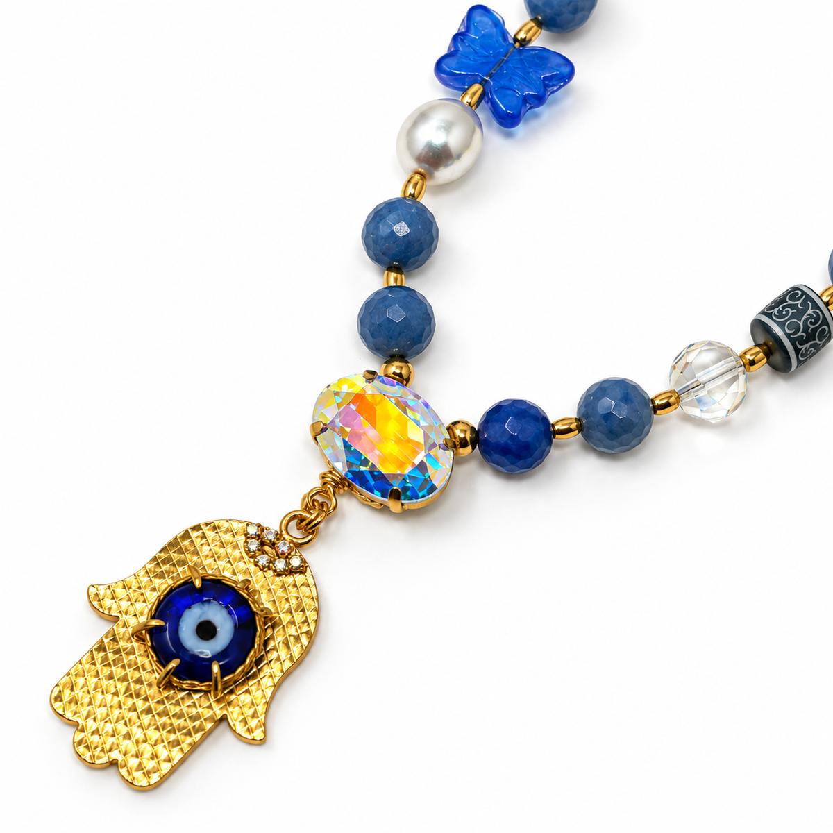 Close-up of the hamsa pendant, blue evil eye, oval crystal, pearl, and blue butterfly detail.