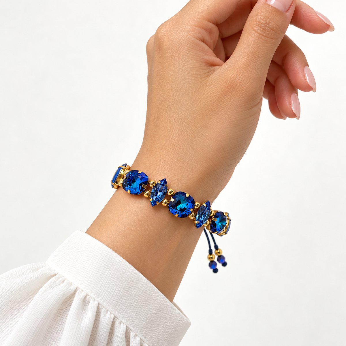Mixed-cut blue Swarovski crystal bracelet with gold-tone settings and an adjustable cord, shown on the wrist.